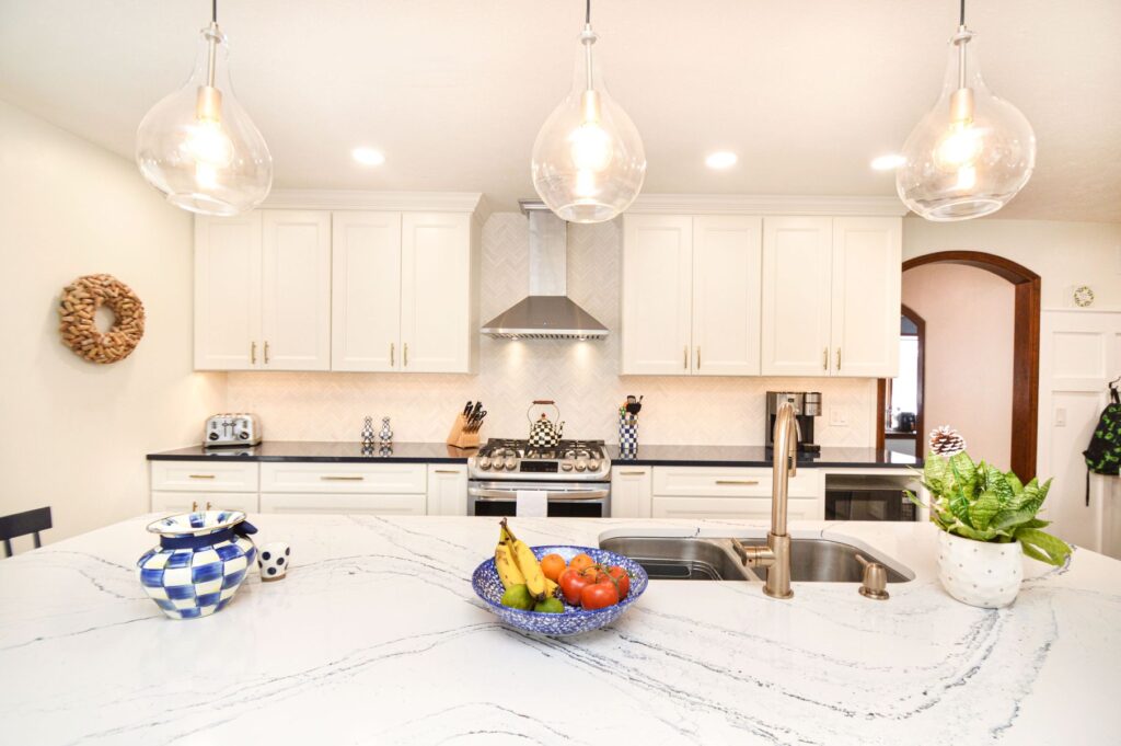 A remodeled rochester ny kitchen with marble countertops and white cabinets. There's a fruit bowl, plant, and decorative vase on the counter