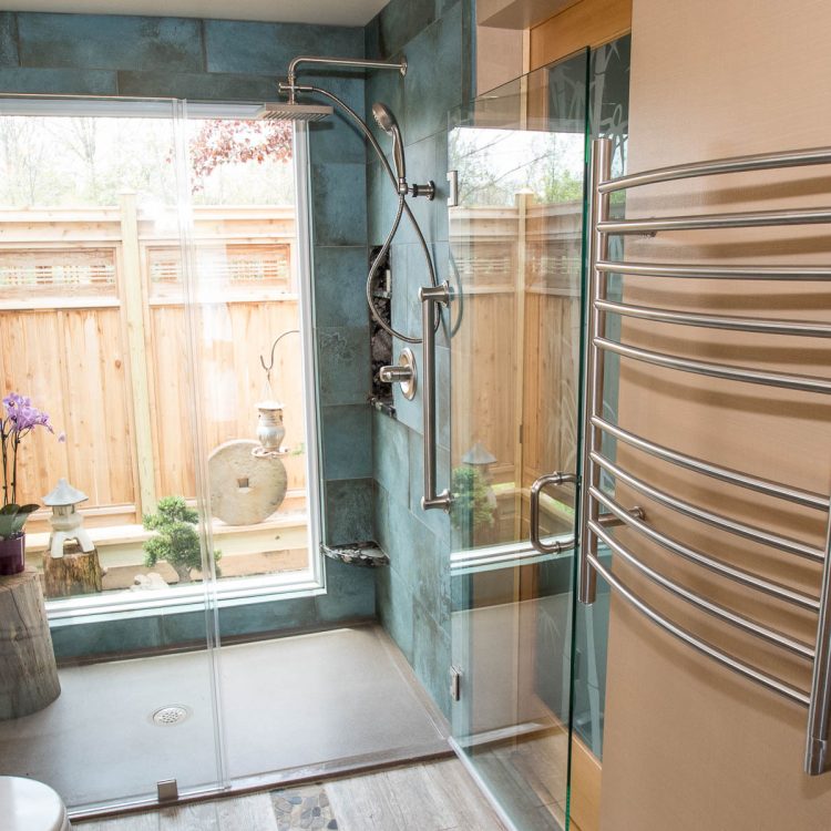 378_Manitou_Road_017 A modern shower with blue-green tiled walls, built-in pebble-tiled niches holding candles, and a sleek metal shower handle. A large window provides a view of a small enclosed outdoor garden with a wooden fence, bonsai tree, stone ornaments, and a hanging lantern. To the right of the shower is a wall with a silver towel rack
