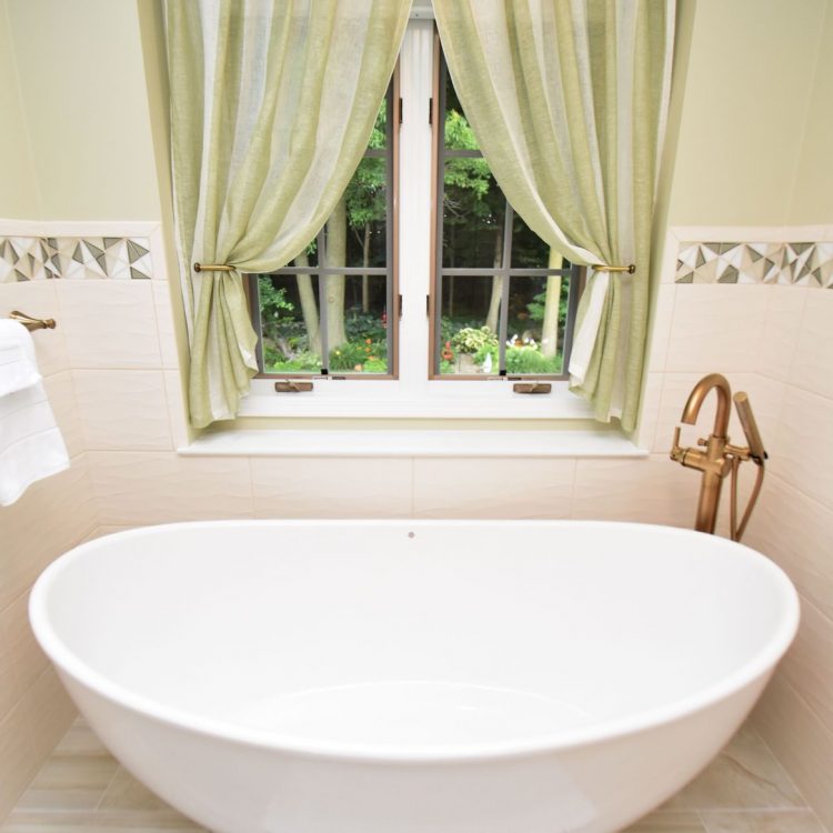Hampshire Lane (14) A renovated bathroom with a bathtub Infront of a window. White tiles are on the bottom half of the wall and green paint covers the top half of the wall